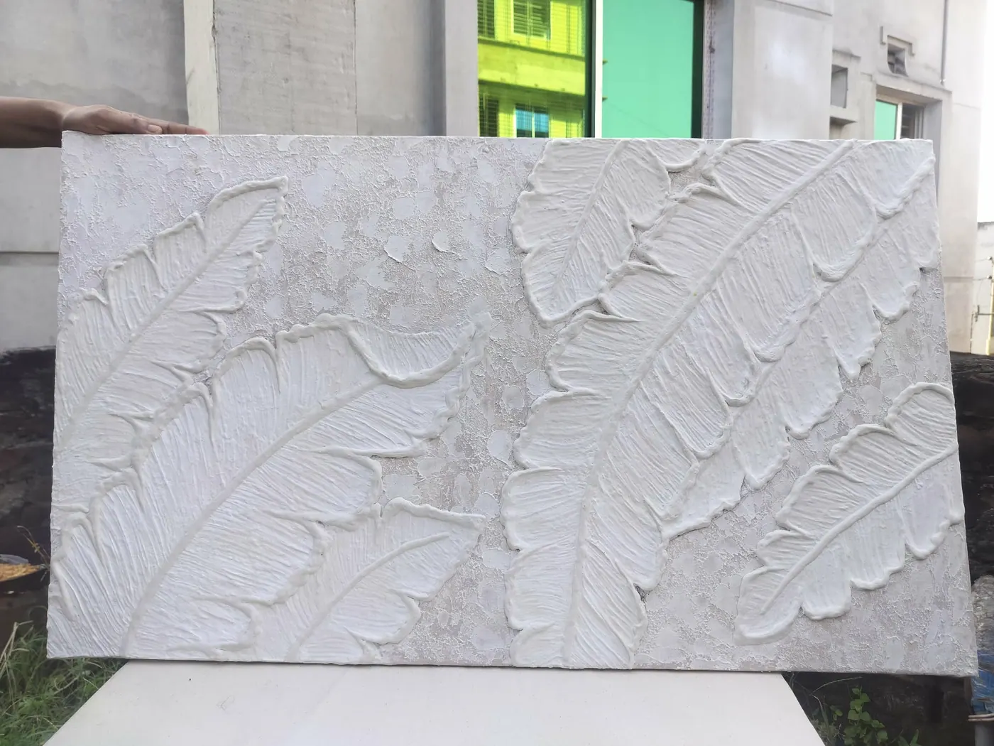 Enlarged detail of all-white relief artwork of large banana leaves on a crackled plaster background